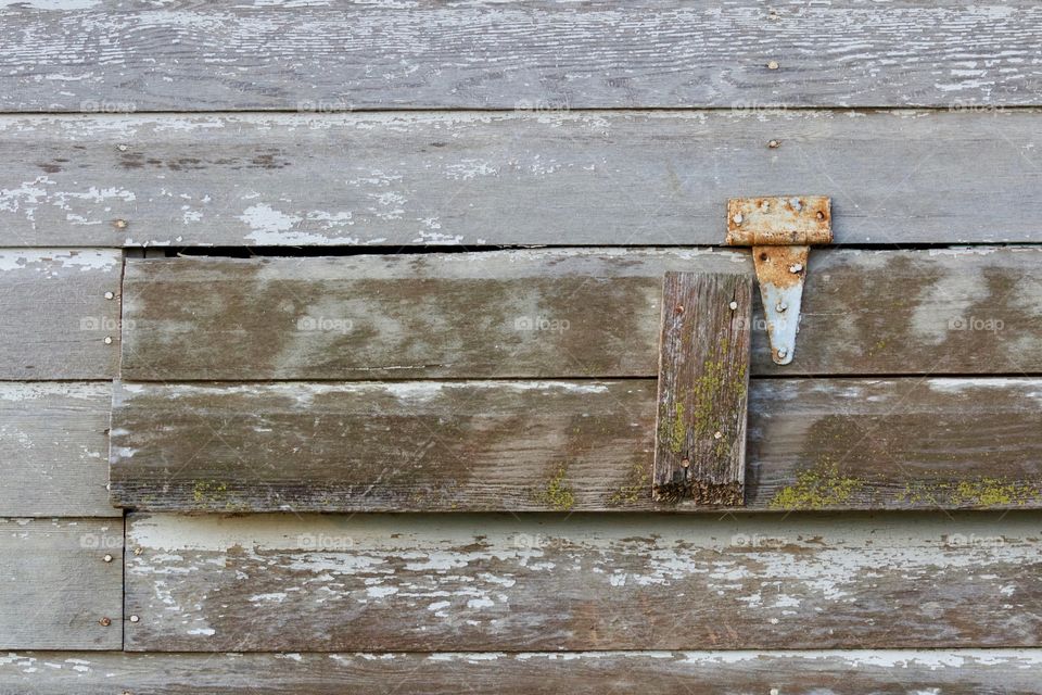 Rusted hinge on a weathered wooden ventilation opening in the siding of an antique farm building  