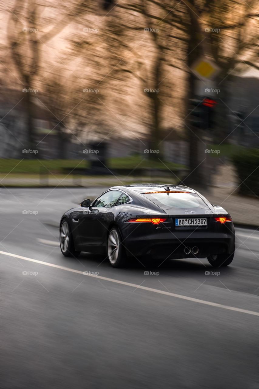 Gray Jaguar sports car with german license plate in europe coming to a stop at intersection with traffic lights in Bochum with orange sky in the background 