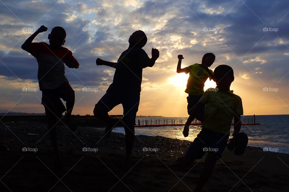 Kids joy is expressed when playing soccer by the beach and with the beautiful sun setting in the back...