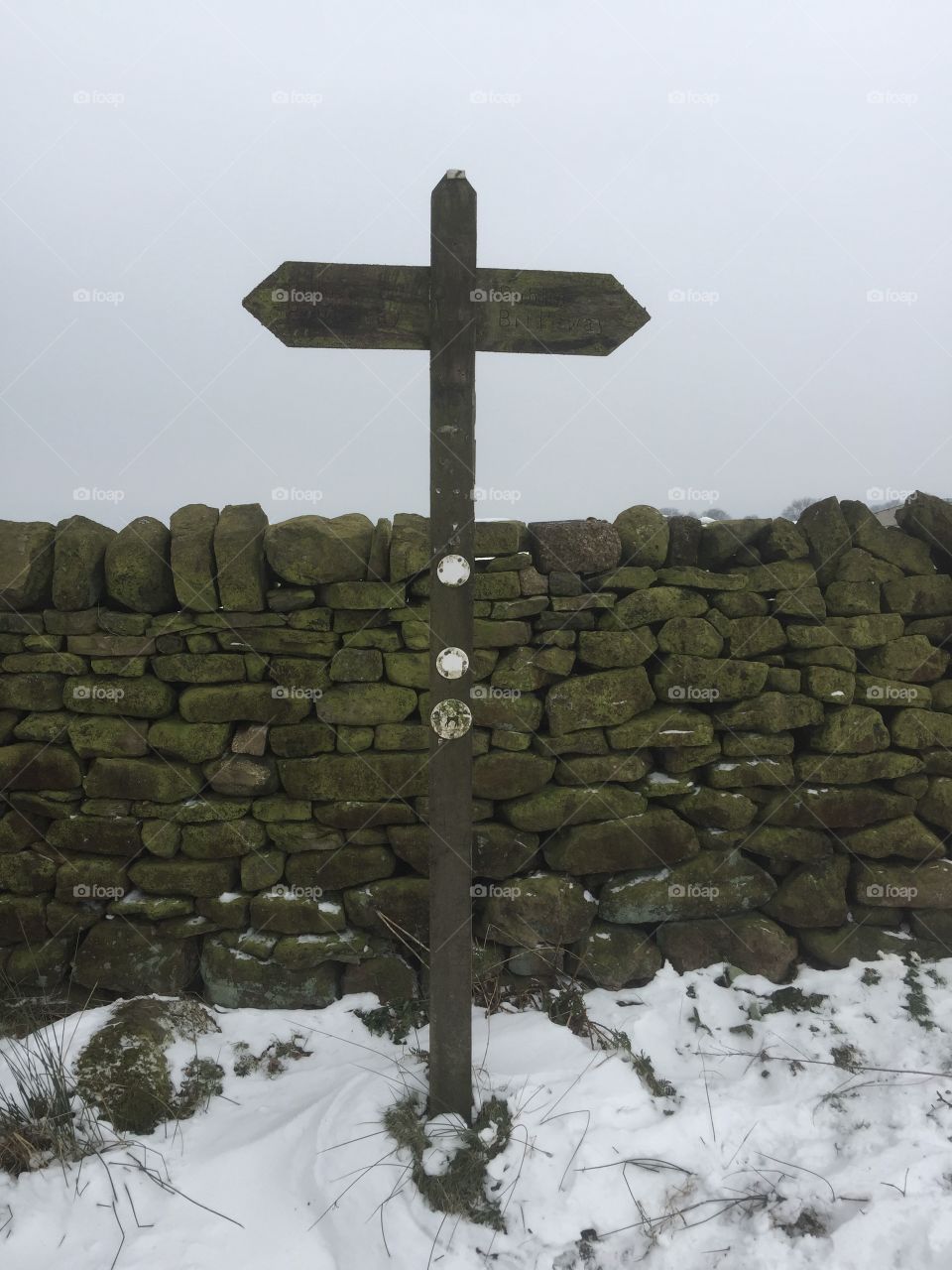 Old signpost and drystone wall in the snow , Yorkshire.