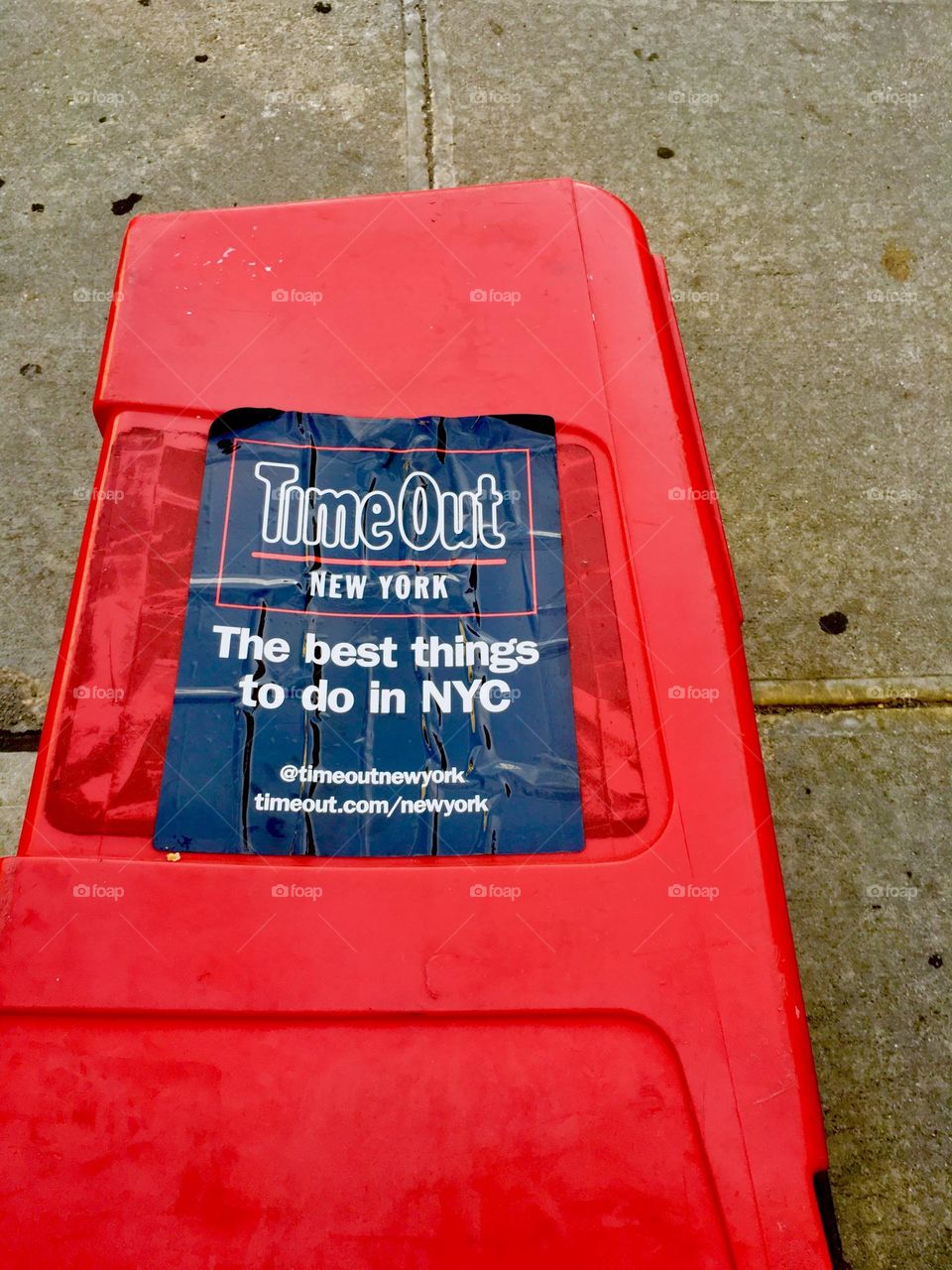 Copies of „Time Out New York“, the magazine is laid out on a LIC sidewalk protected by a bright red plastic cover with a black label. 2020. Hypnotic Productions