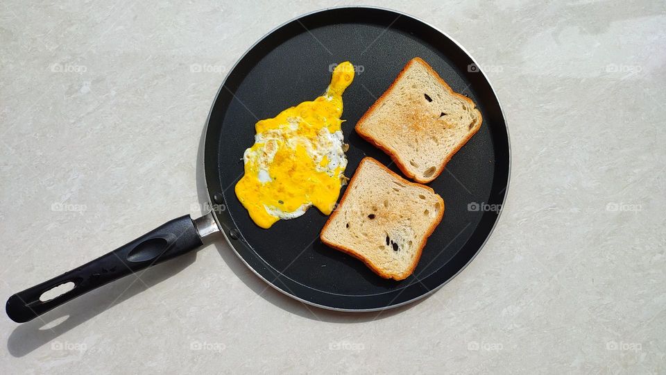 A metal pan (non-stick pan) with a simple omelette and two toasted breads on sides