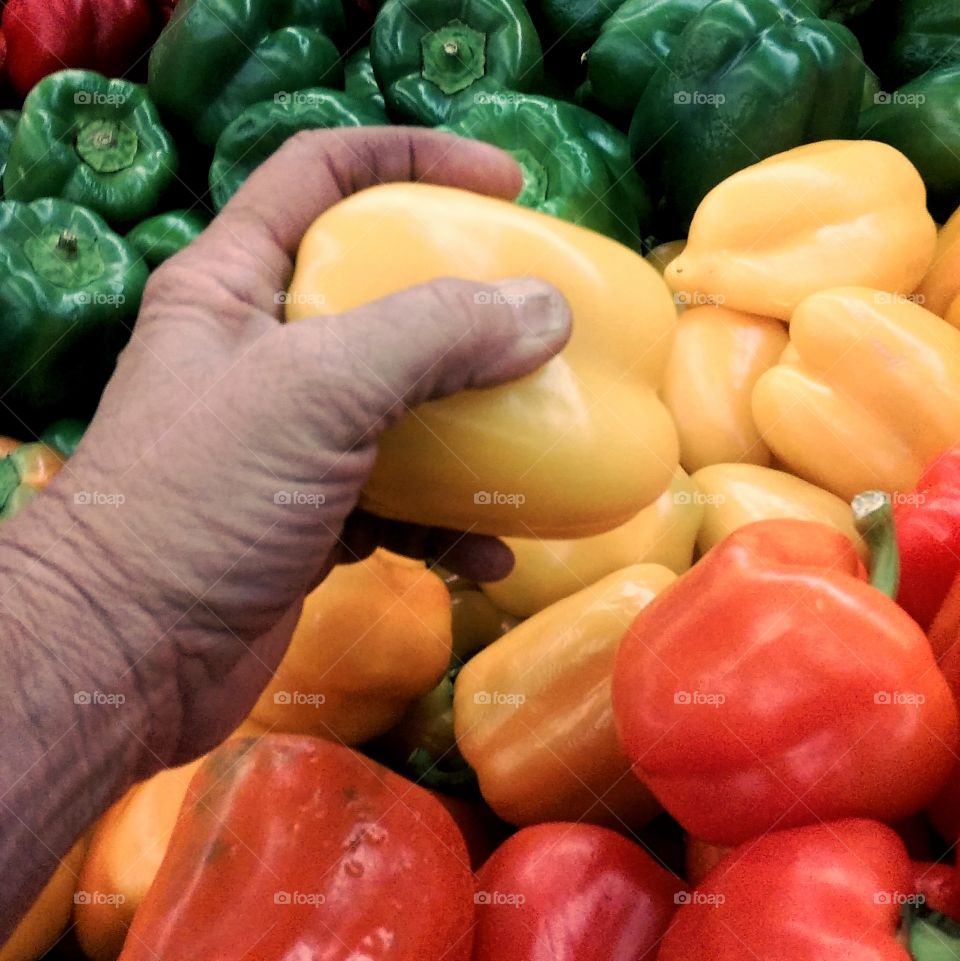 food in hand wrinkled old woman hand yellpw pepper green red pepper in background