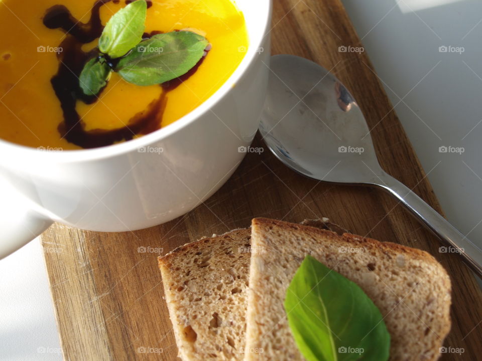 delicious and hot pumpkin soup decorated with basil and fresh bread on the side