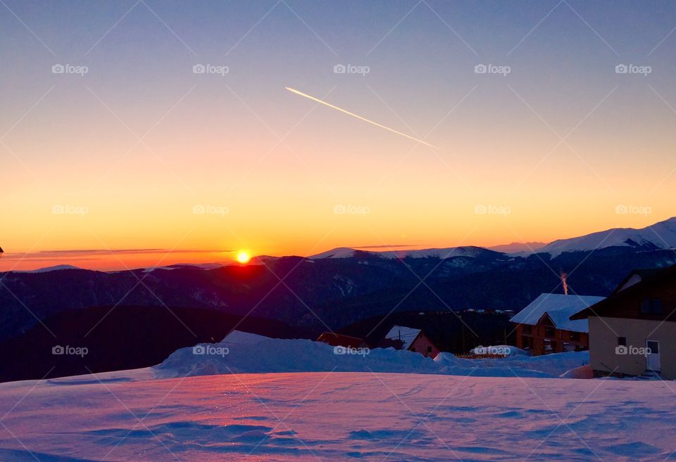 Sunset in winter in the mountains with plane flying on the sky