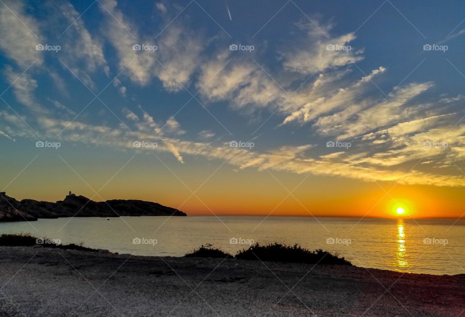 Beautiful feathery encrustations stretching diagonally across the entire sky with the sun setting over the horizon on the Mediterranean Sea of ​​the island of Frioul in France, side view, close-up. Concept beautiful sky wallpaper.