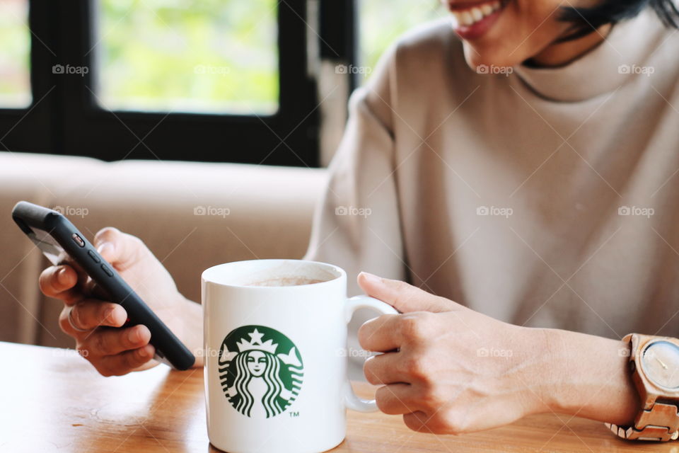 woman smiling while playing mobile phone and hold the sturbucks mug