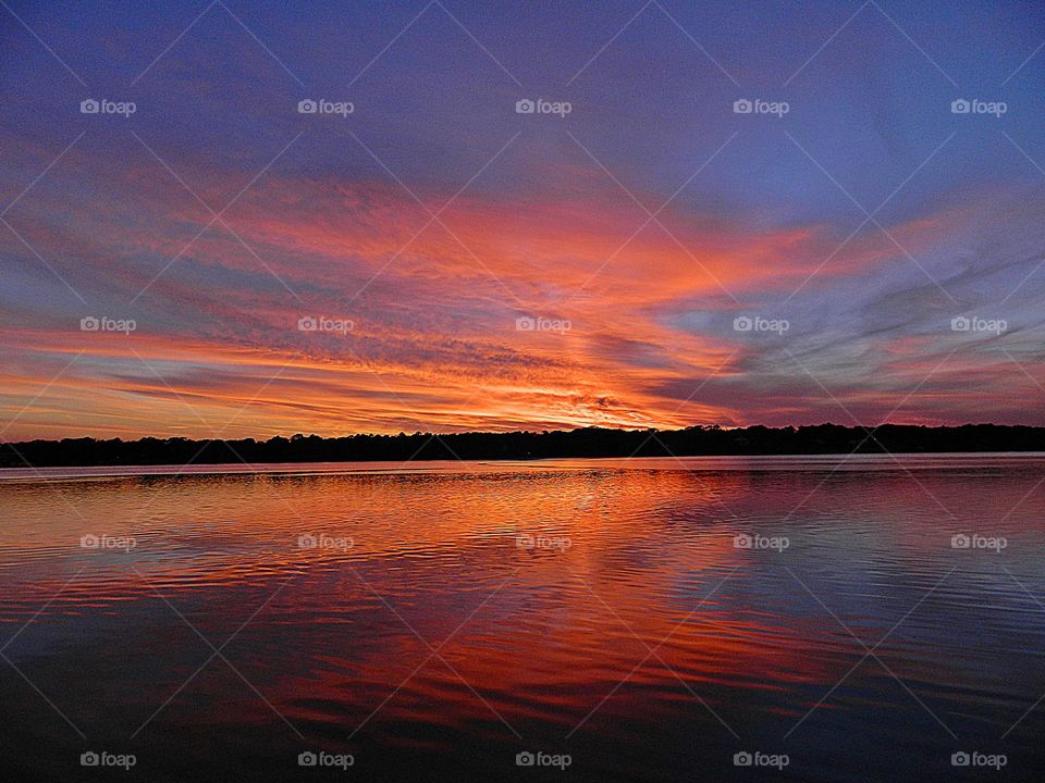 Clouds - Magnificent multicolored clouds in the blue sky reflect on the shimmering surface of the calm water
