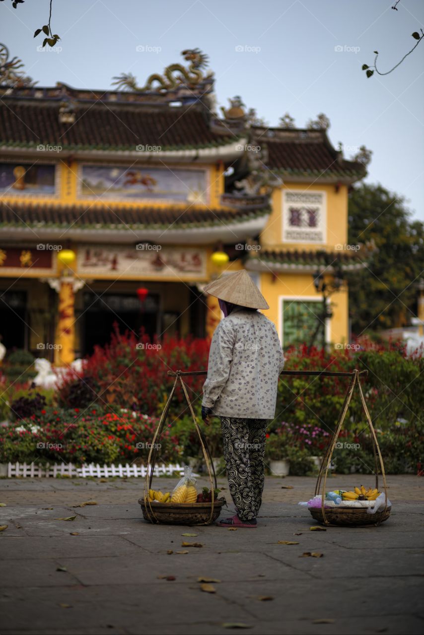 typical scene in Hoi An ancient town, old lady wearing conical hat and traditional costum in front if buddhist temple in central Vietnam