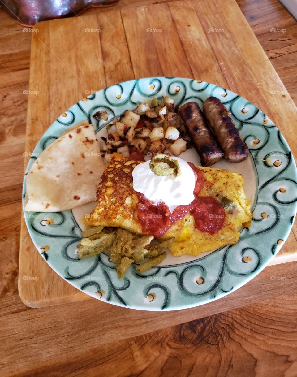 An omelet stuffed with cheese,  vegetables and meat with sausages, o'Brien potatoes,  a tortilla, with fried jalapenos makes for a hearty breakfast.