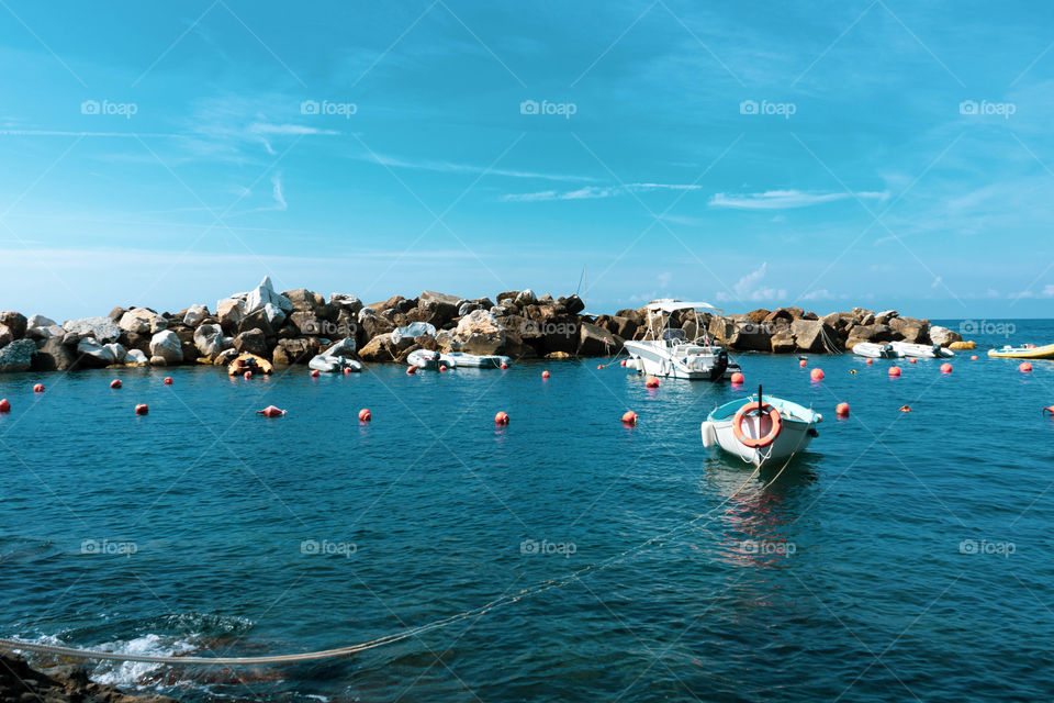 The sea view from the Cinque Terre. The boats sail between the waters and the rocks. A small house overlooking the sea colors the view.