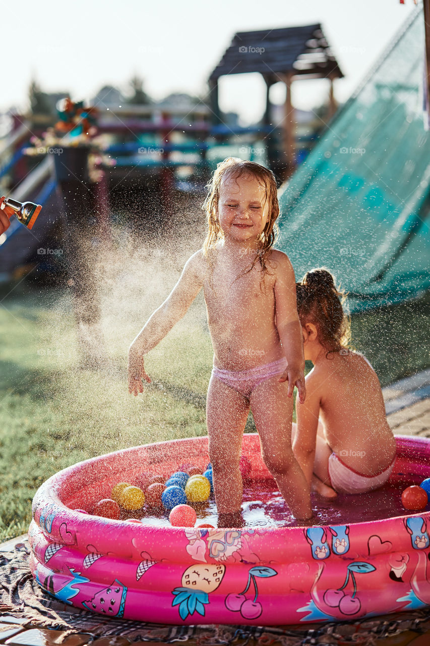 Little cute adorable girls enjoying a cool water sprayed by their father during hot summer day in backyard. Candid people, real moments, authentic situations