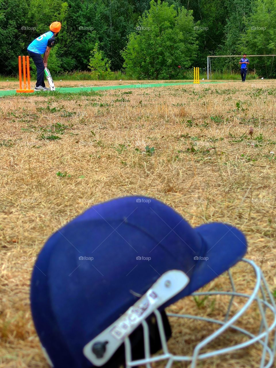 cricket training.  two players prepare to throw the ball.  in the foreground of the photograph a protective helmet for playing cricket lies on the field