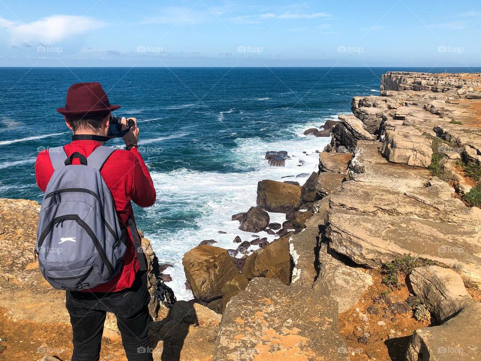 A hiker with a backpack pauses to photograph the jagged, jurassic coastline at Peniche, Portugal 