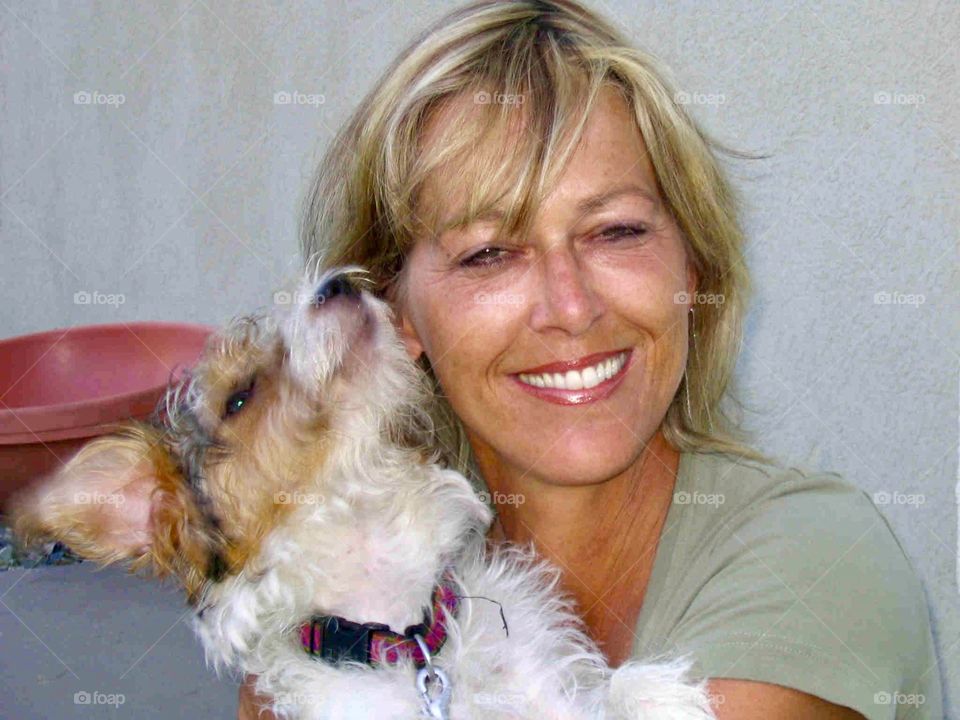 Blonde middle aged woman smiling while holding her young jack Russell terrier pet close to her face 