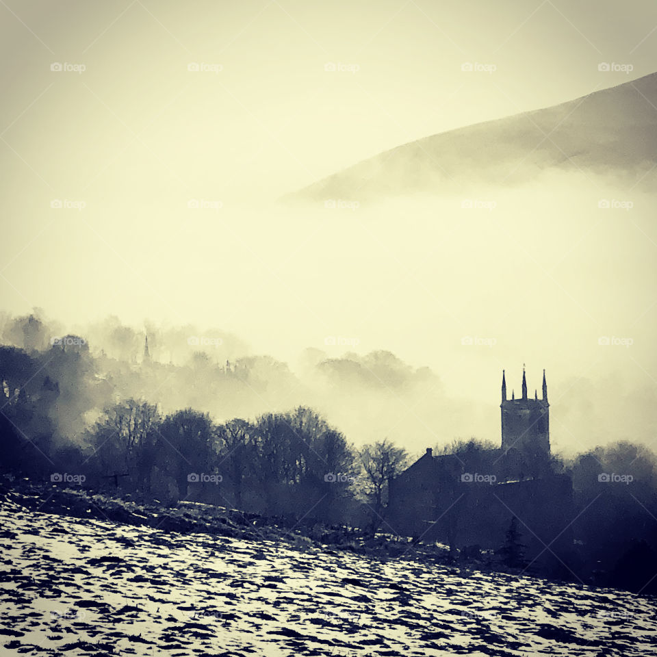 Moody landscape with church spire surrounded by mist