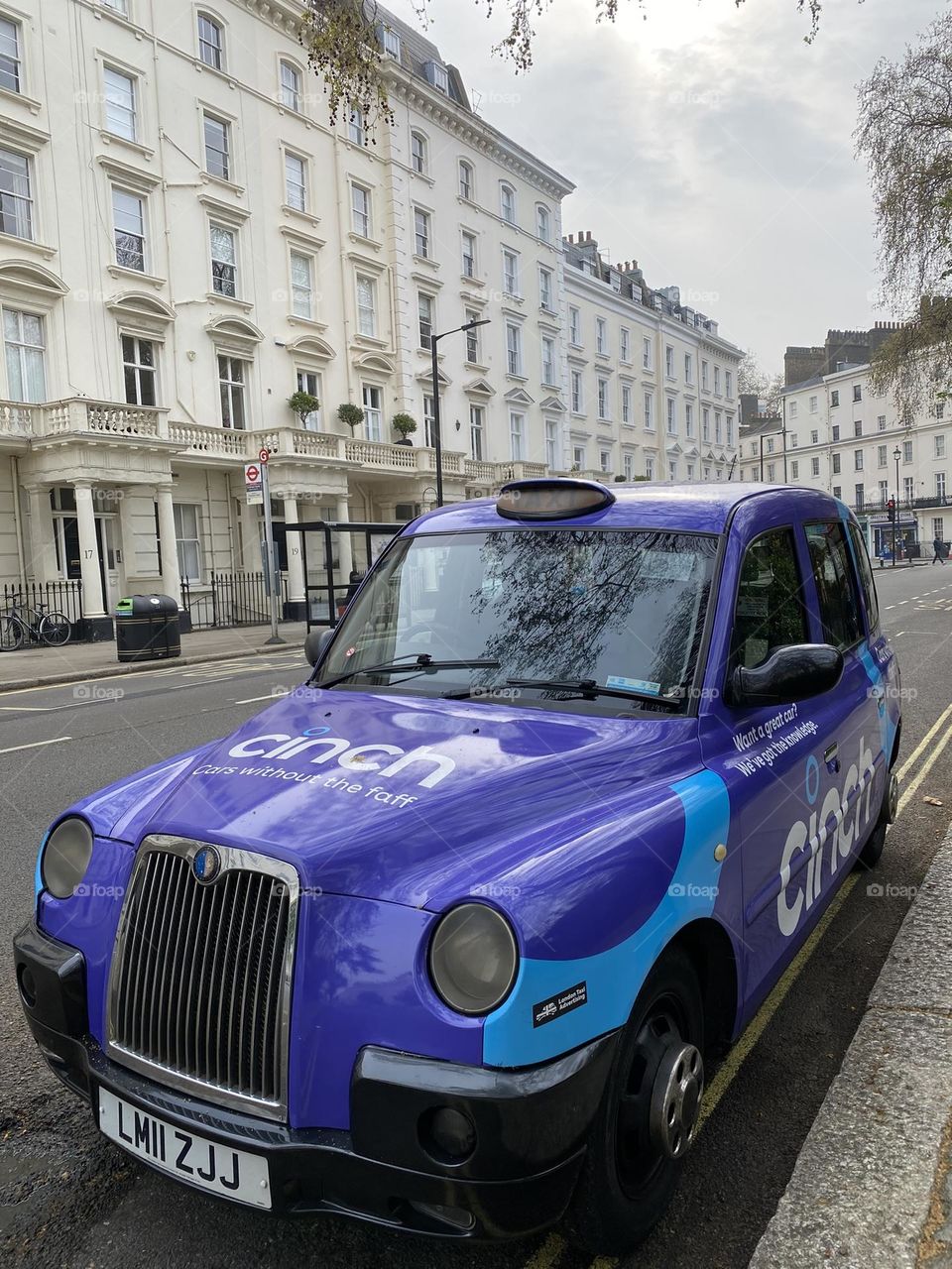 Purple taxi parked in London street along white elegant buildings.