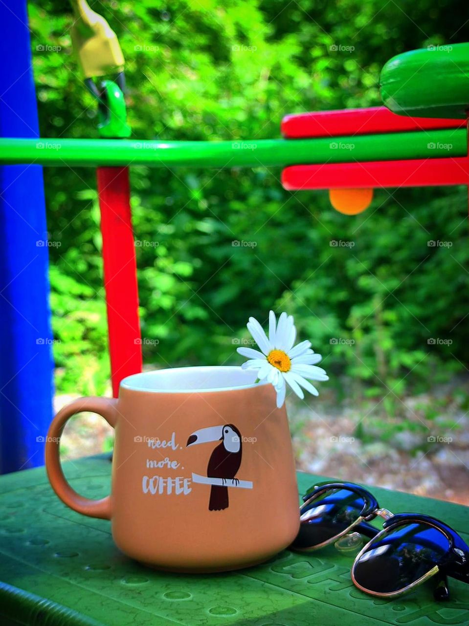 Summer. There is a coffee mug with a funny pattern on the swing. There is a camomile in the mug. There are sunglasses next to the mug.