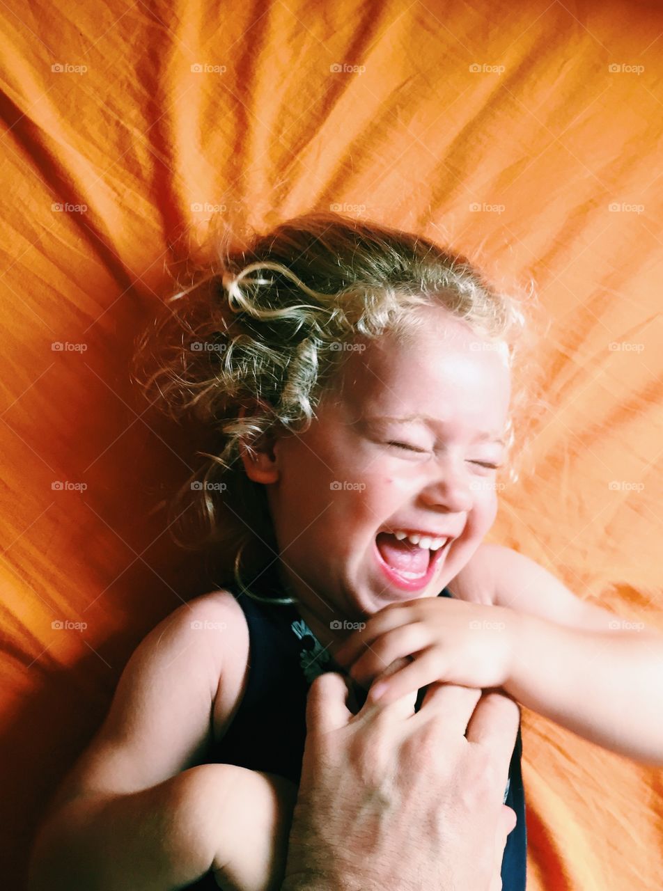 High angle view of little girl lying on bed and laughing