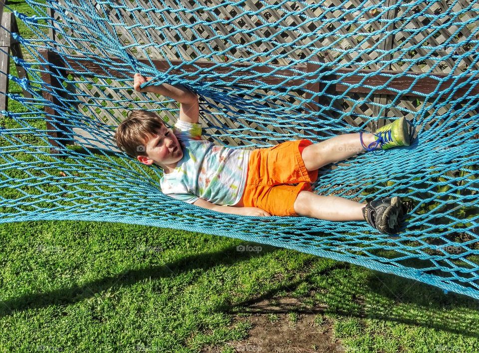 Little Boy Swinging In A Blue Hammock. Backyard Fun
