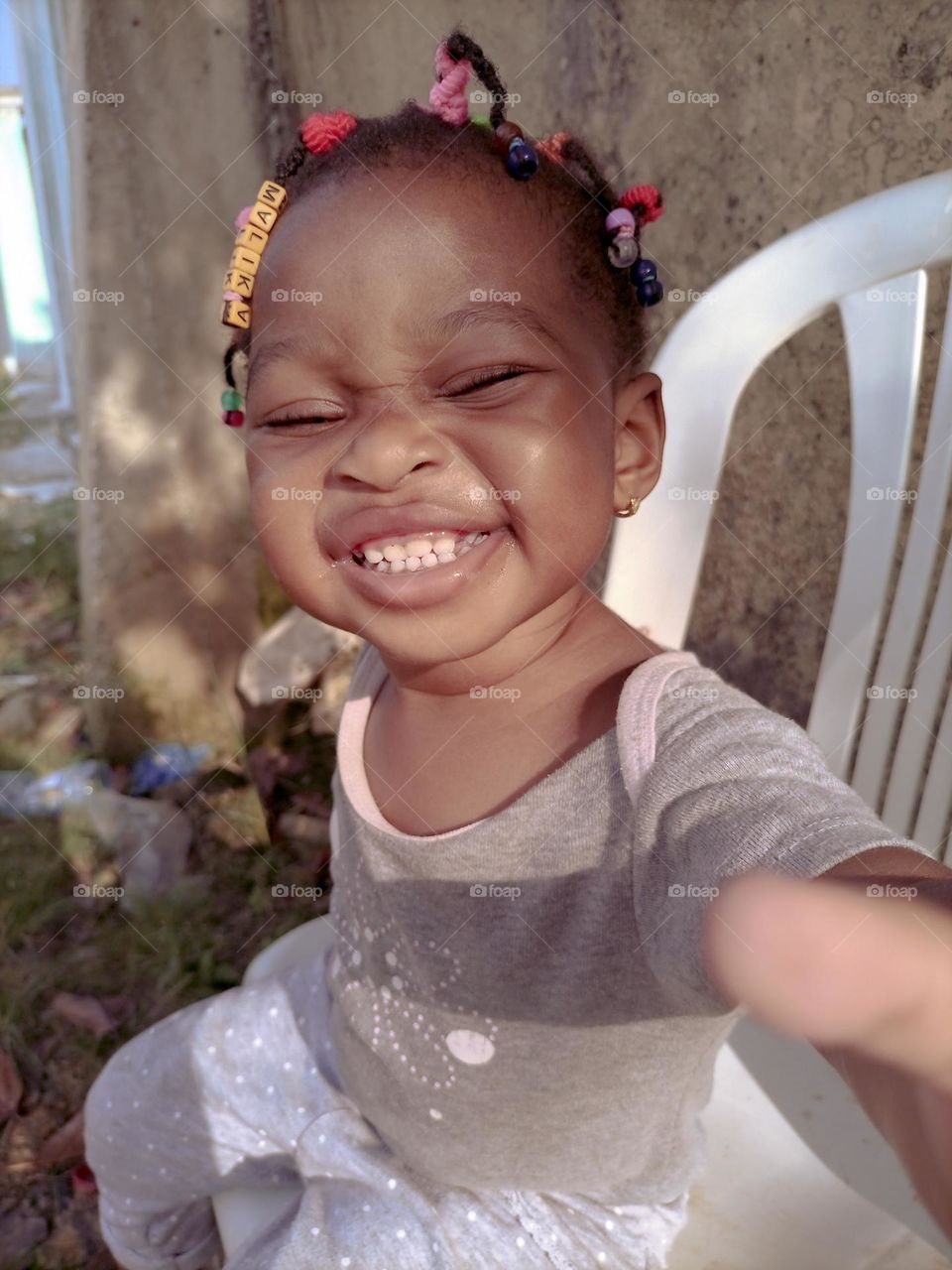 a beautiful baby sitting on a chair who smiles at the camera and wants to take it.