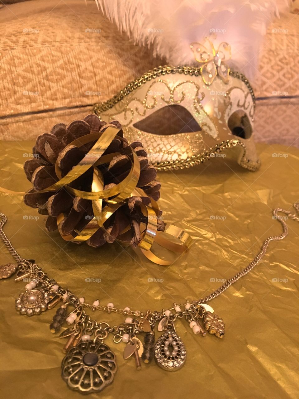 Gold charm necklace with a pinecone swirled in gold curling ribbon with a gold Venetian masquerade mask 