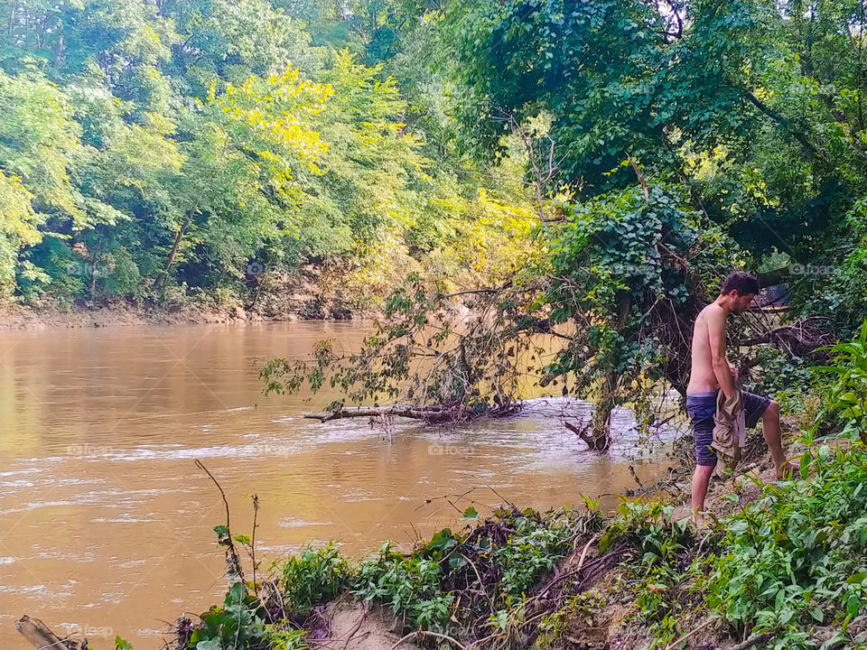 Man in bathing suit climbing up riverbank after a swim.