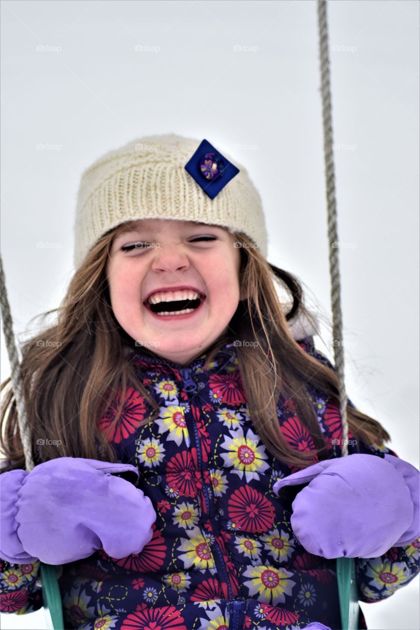 little girl laughing as she swings in the winter