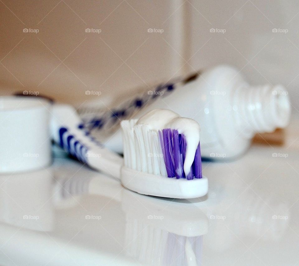 Stock photo of purple, white and blue toothbrush with white toothpaste in bathroom