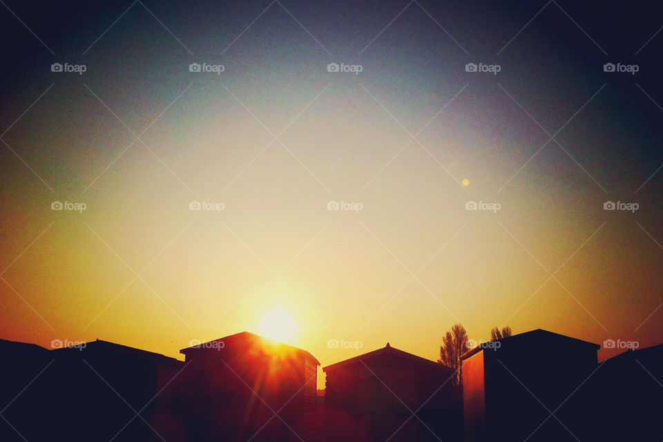 THE SUN SETTING BEHIND A ROW OF ENGLISH BEACH HUTS.