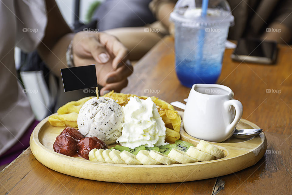 Sweet water pour on the waffle with ice cream and fruits including bananas, kiwi and strawberries in wooden plate on table.