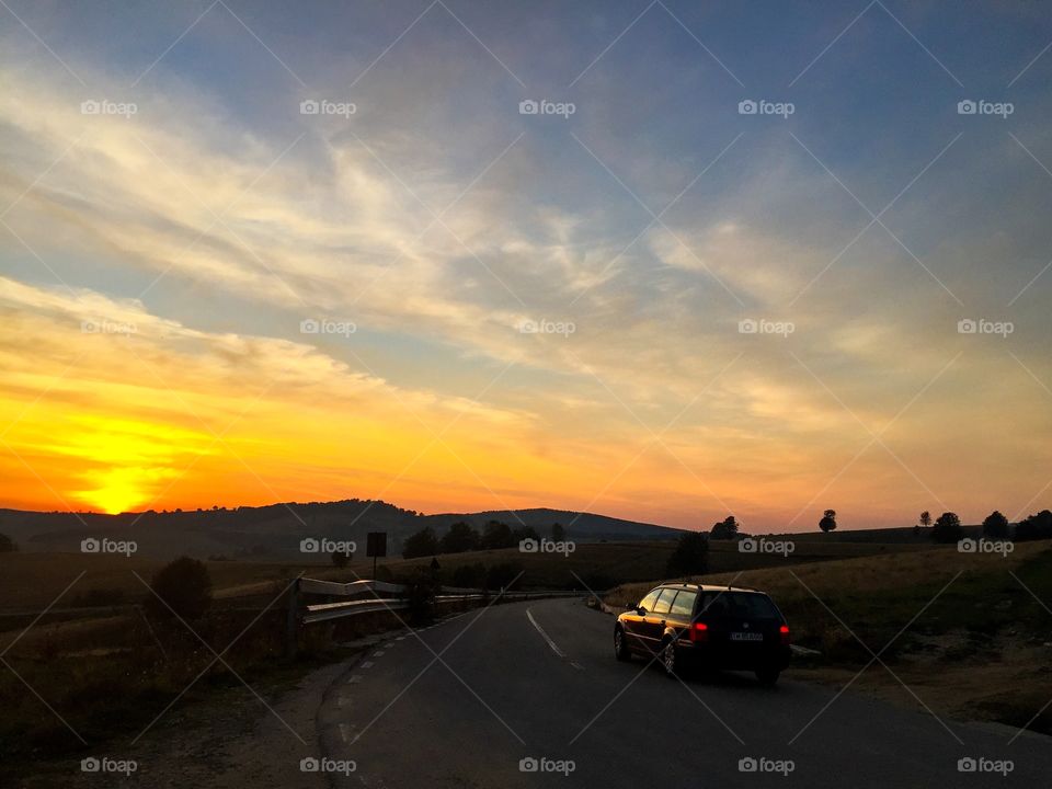 Car driving on an empty road in the mountains during golden hour in summer