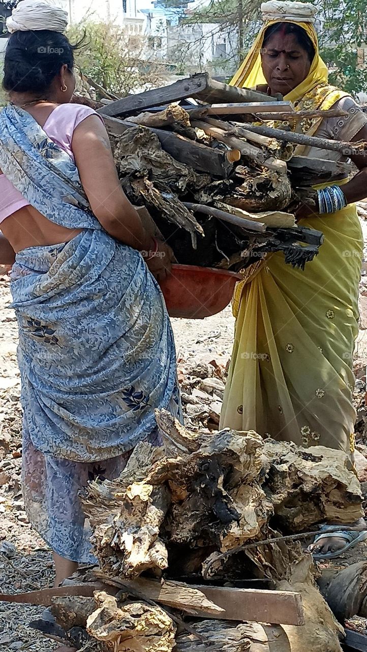 two ladies helping each other in uploading there weight of wood pieces tub one by one