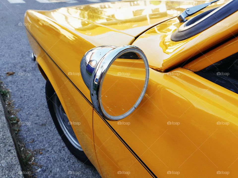Close-up photo of circular side view mirror on a yellow vintage car