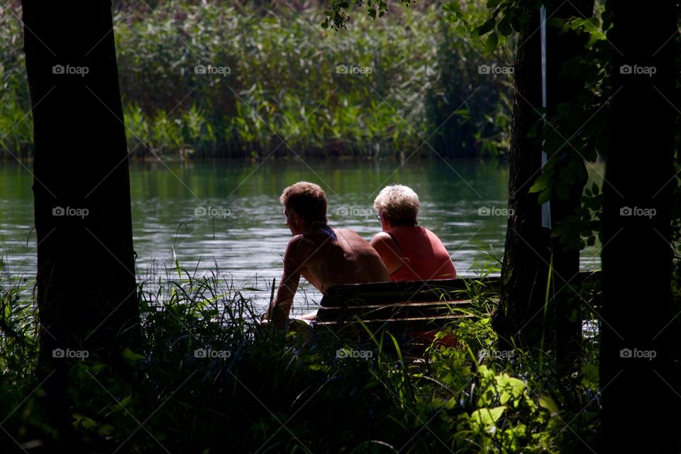 Couple Sitting On Bench By The Lake