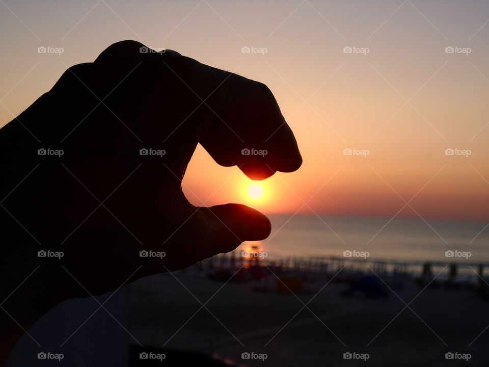 Hand holding sun between fingers at sunrise at the seaside