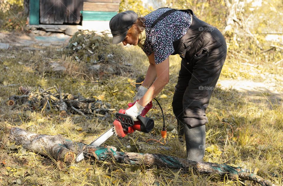 A woman cuts wood with an electric chainsaw