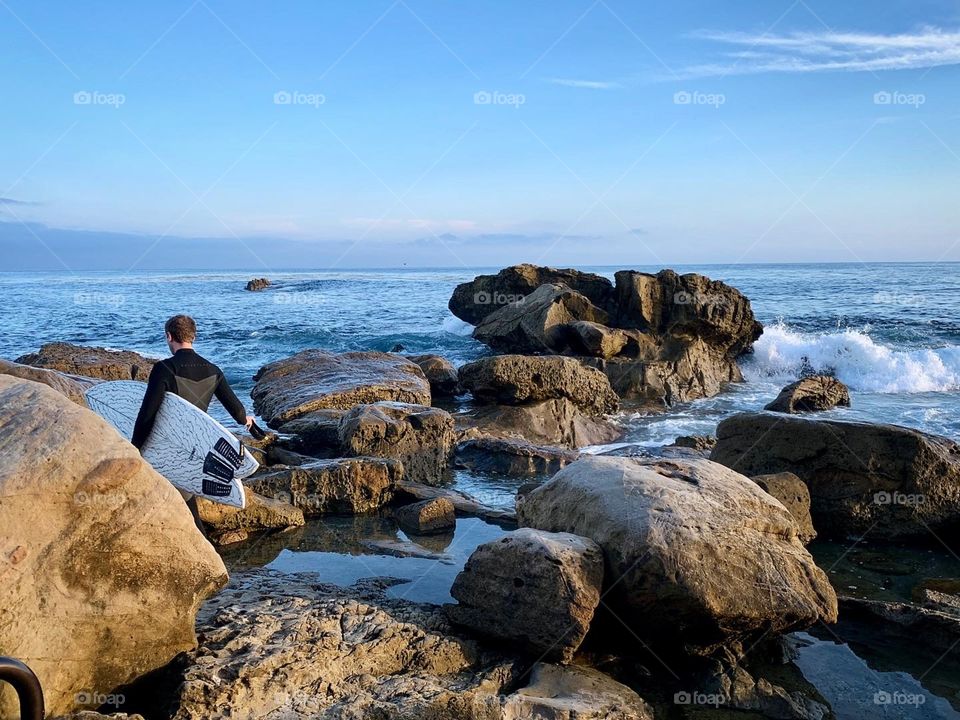 Surfer walking through the tide pools to get into the ocean