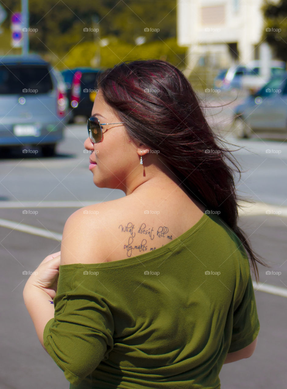Young woman showing her text tattoo on her back