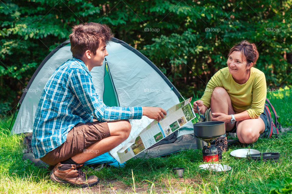 Spending a vacation on camping. Woman preparing a meal outdoor. Man holding a map. Planning next trip