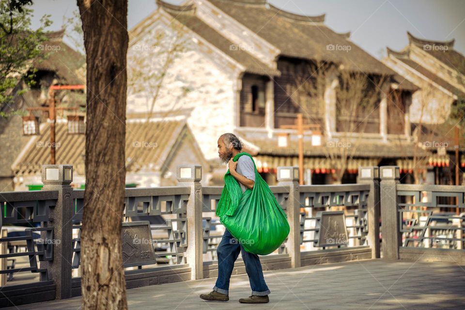 A man is carrying his green bag to acculturate the residual.