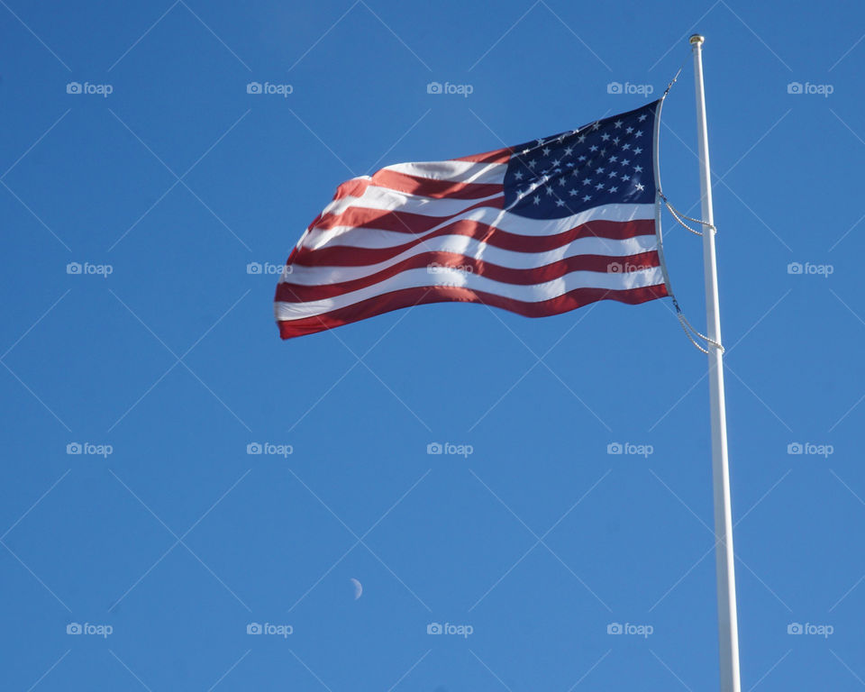 Flag blowing in the wind with the moon during the day