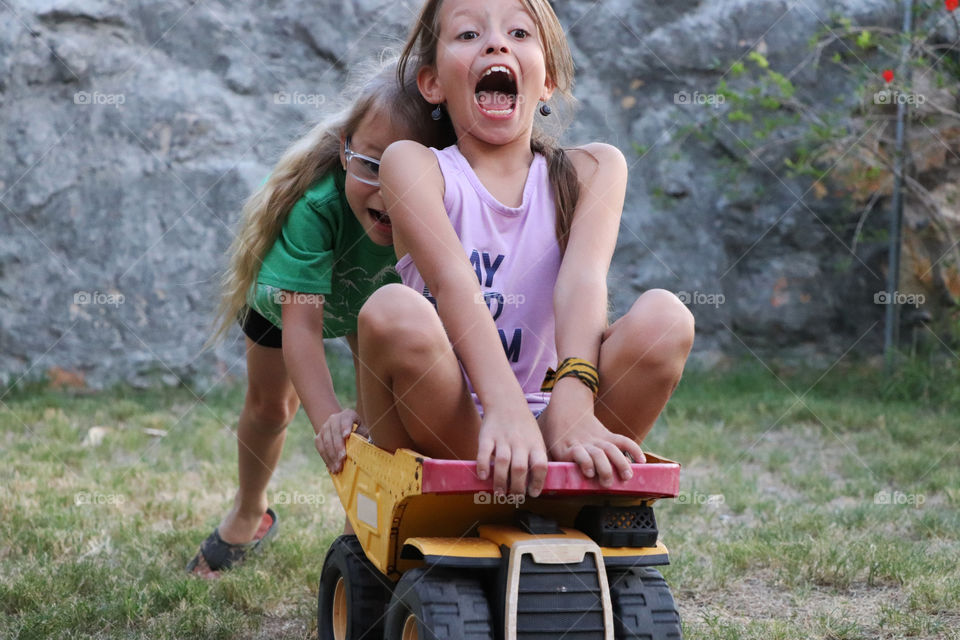 Younger sister pushing her older sister in a toy truck