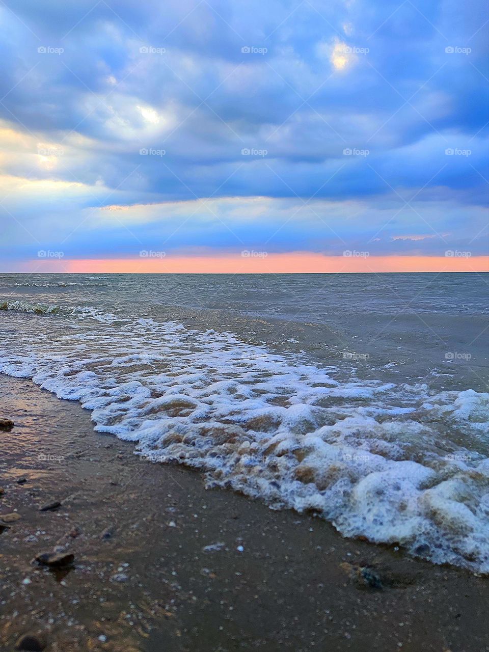 Summer sea. Calm on the sea, small waves turn white near the shore. The sunset colors the clouds in the sky blue. The sky is tinted pink on the horizon