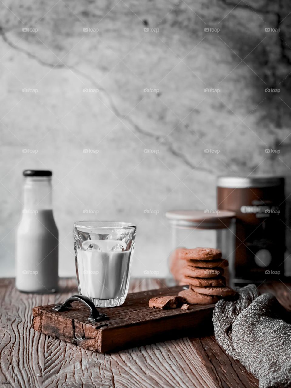Stack of cookies and a glass of milk on a wooden table with blurry milk bottle and biscuits' jar at the background 