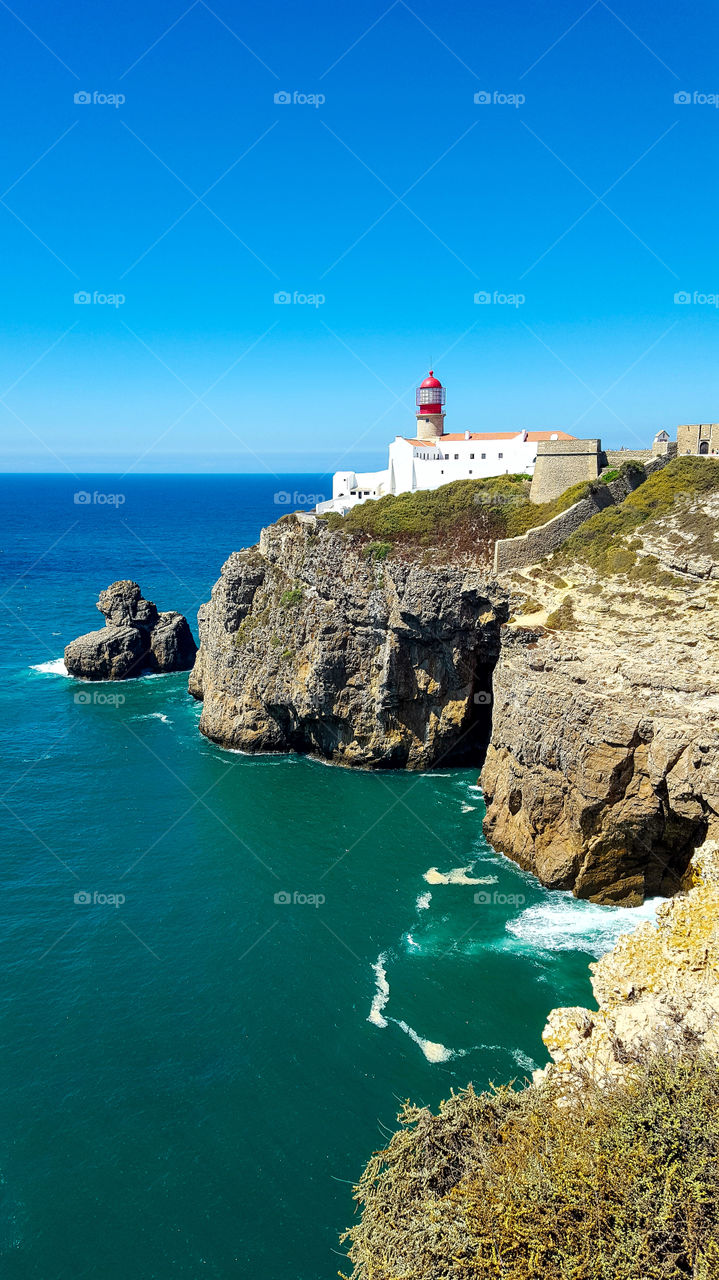 The Cabo de San Vicente Lighthouse (in Portuguese: Farol do Cabo de São Vicente) is a lighthouse located on the Cape of San Vicente, a freguesia of Sagres, council of Vila do Bispo, Algarve region, Portugal. It is built inside the Fortress of San Vicente of the sixteenth century. The headlight emits a flash of white light of 0.1 s of duration every 5 seconds. It has a nominal night range of 32 nautical miles. During the reign of Manuel I of Portugal, at the beginning of the 16th century, the Bishop of Algarve, Fernando Coutinho, ordered a fortress and a tower to be built on the Cape of San Vicente as a beacon as a defense of that area of the coast. In 1587, the British pirate Francis Drake destroyed the fort and the primitive lighthouse. The structure was ordered to be rebuilt by King Felipe II of Portugal, (III of Spain) in 1606. Like all the fortresses in the area, it was razed during the earthquake of 1755.