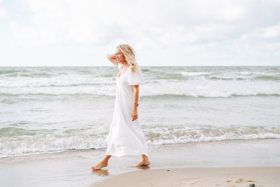 Young blonde beautiful woman with long hair in white dress enjoying life on the sea beach