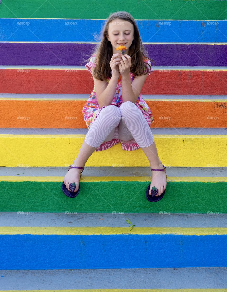 Girl smells orange flower on rainbow-coloured stairs