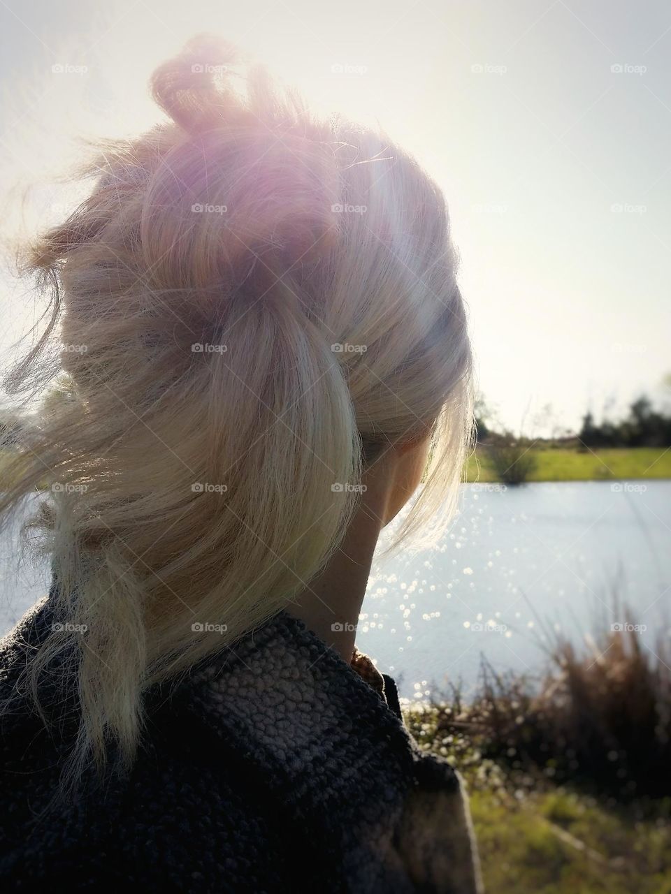 Woman from the back with blond hair looking at water as the sun goes down