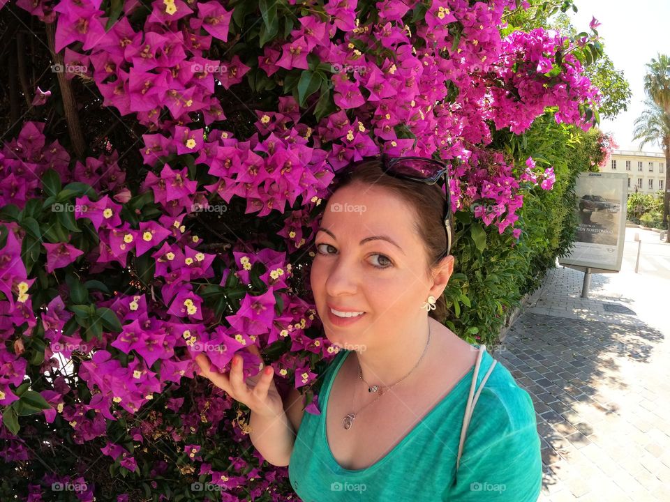 A smiling girl with Green top agains a wall of pink purple flowers